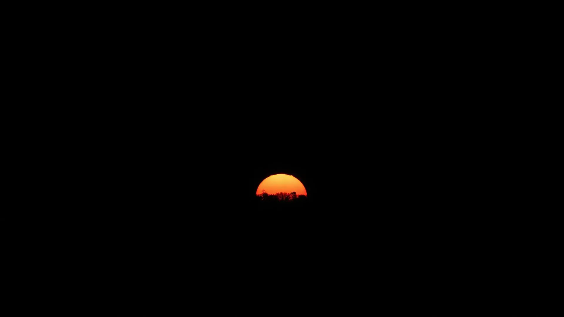 Sunrise emerging from darkness over a distant horizon